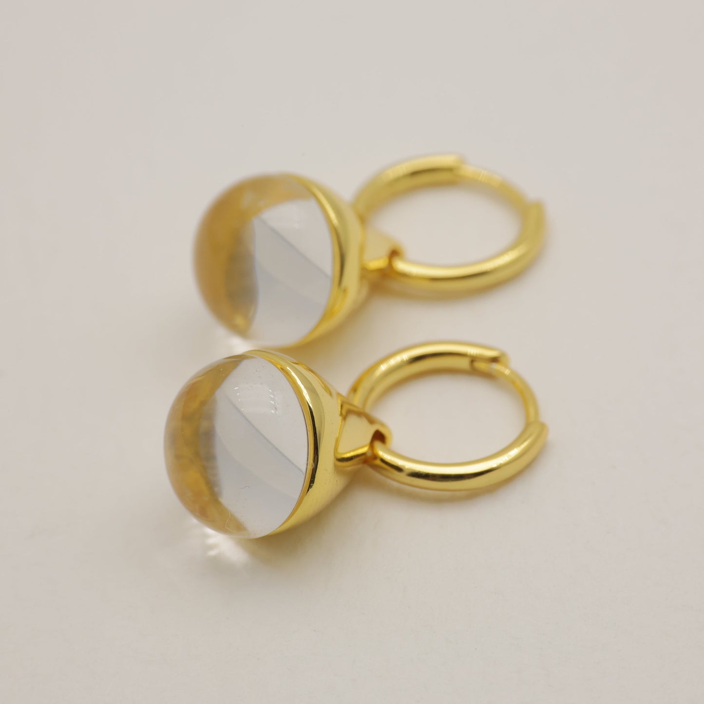 Gold hoop earrings with a clear stone on a light beige background