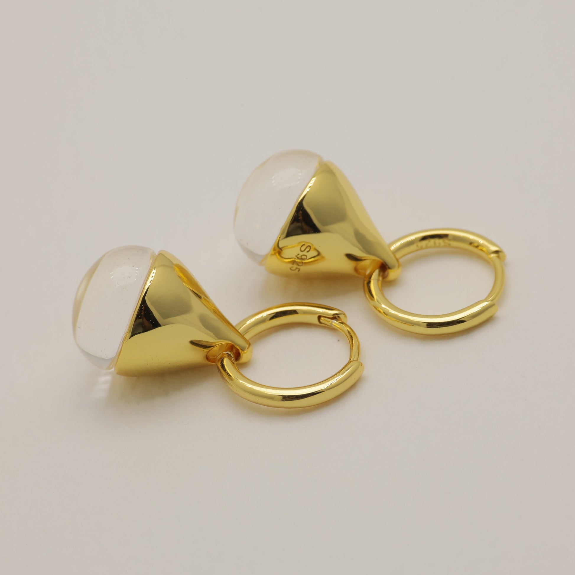 Gold earrings with a clear gemstone on a light gray background