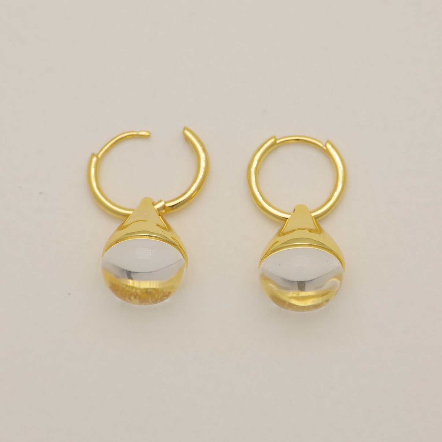 Pair of gold hoop earrings with white stones on a beige background