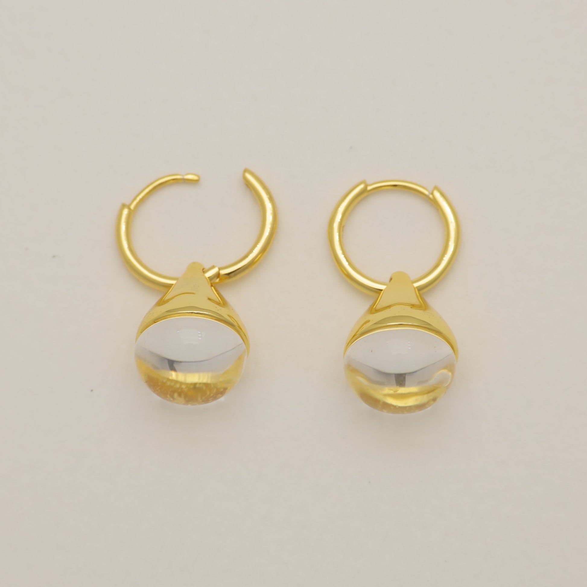Pair of gold hoop earrings with white stones on a beige background