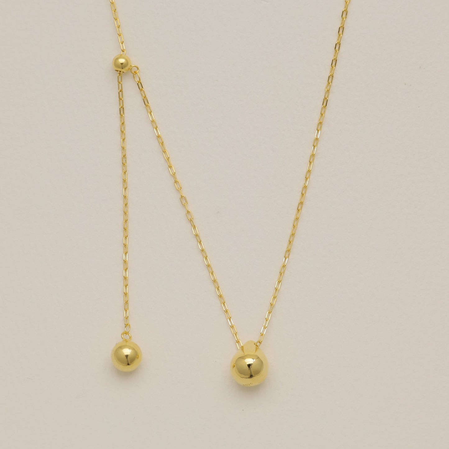 Gold necklace with small round pendants on a light beige background