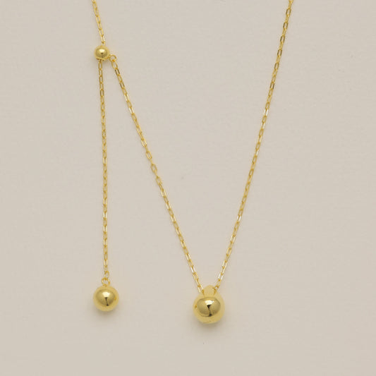 Gold necklace with small round pendants on a light beige background