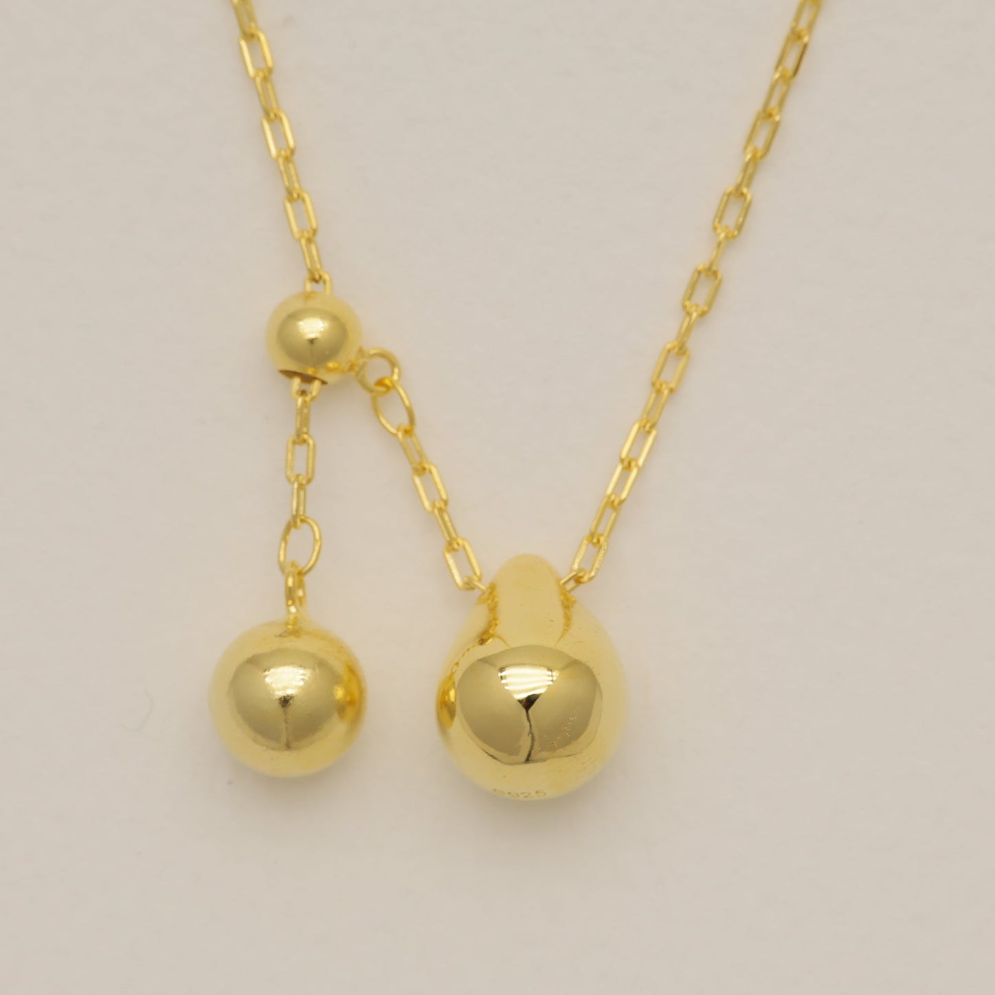 Gold necklace with spherical pendants on a beige background