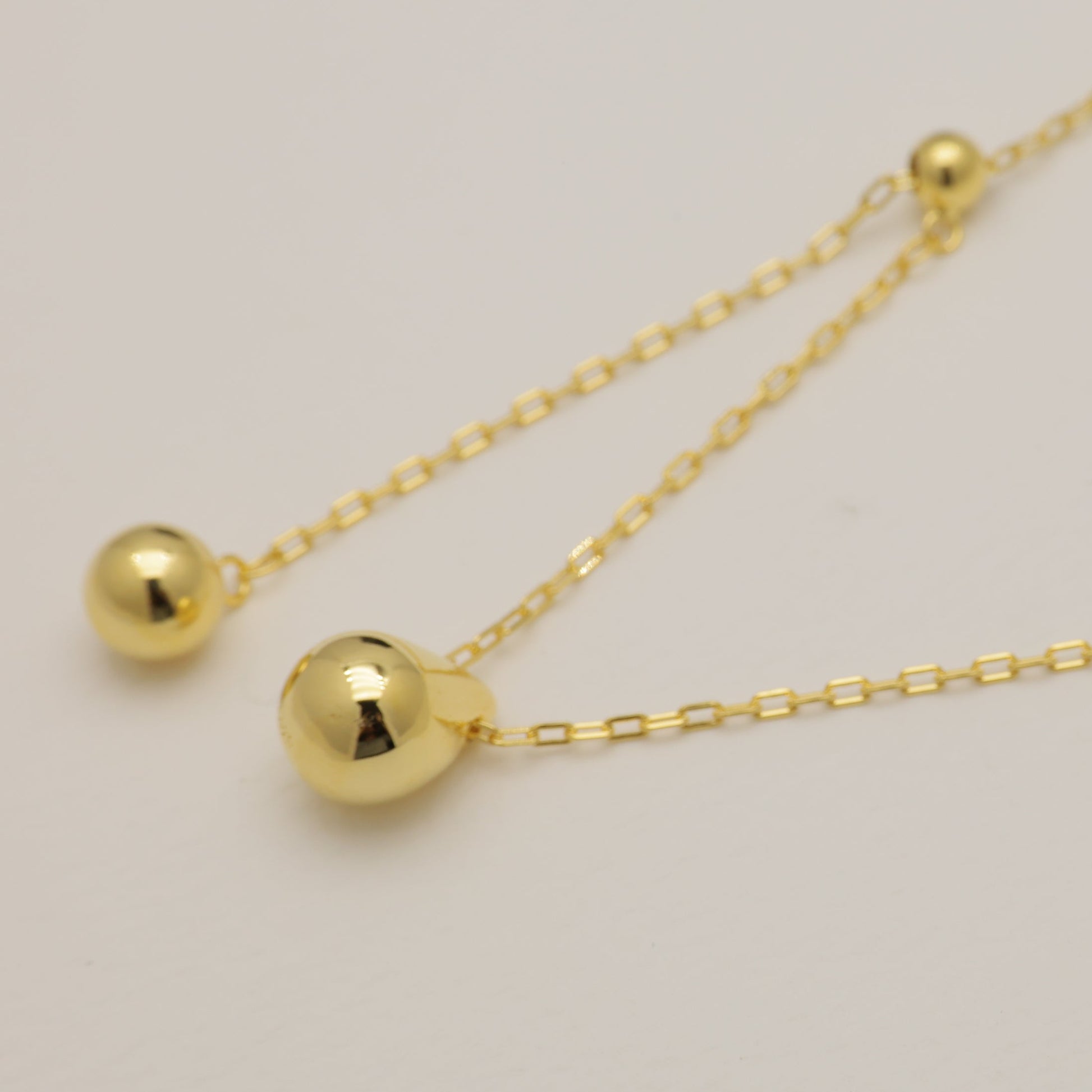 Gold necklace with two spherical pendants on a light gray background
