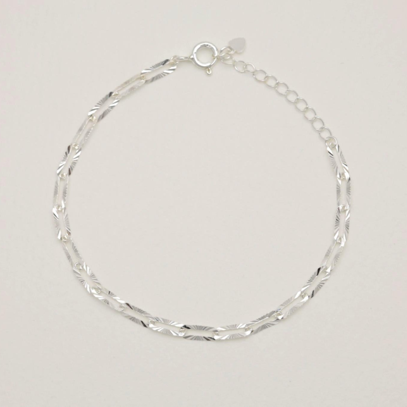 Sterling silver bracelet with engraved oval links laid flat on neutral background