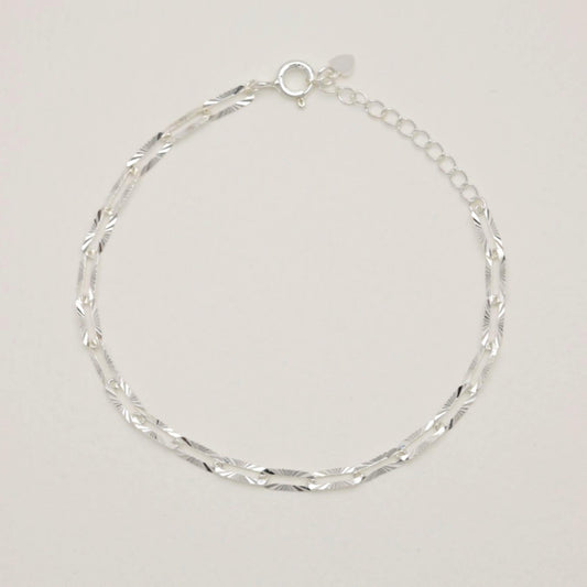 Sterling silver bracelet with engraved oval links laid flat on neutral background
