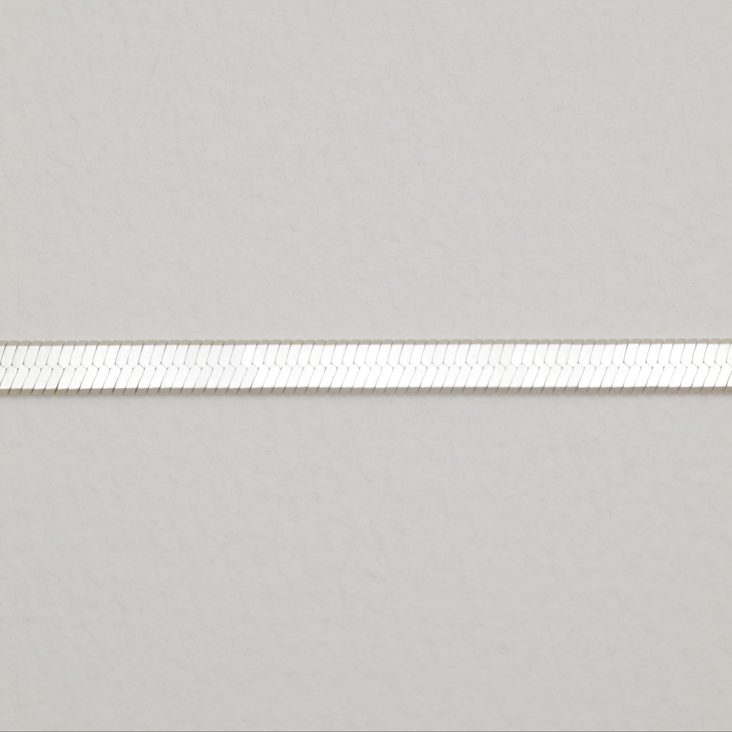 Close-up view of the silver herringbone chain pattern, showing its smooth, reflective surface.