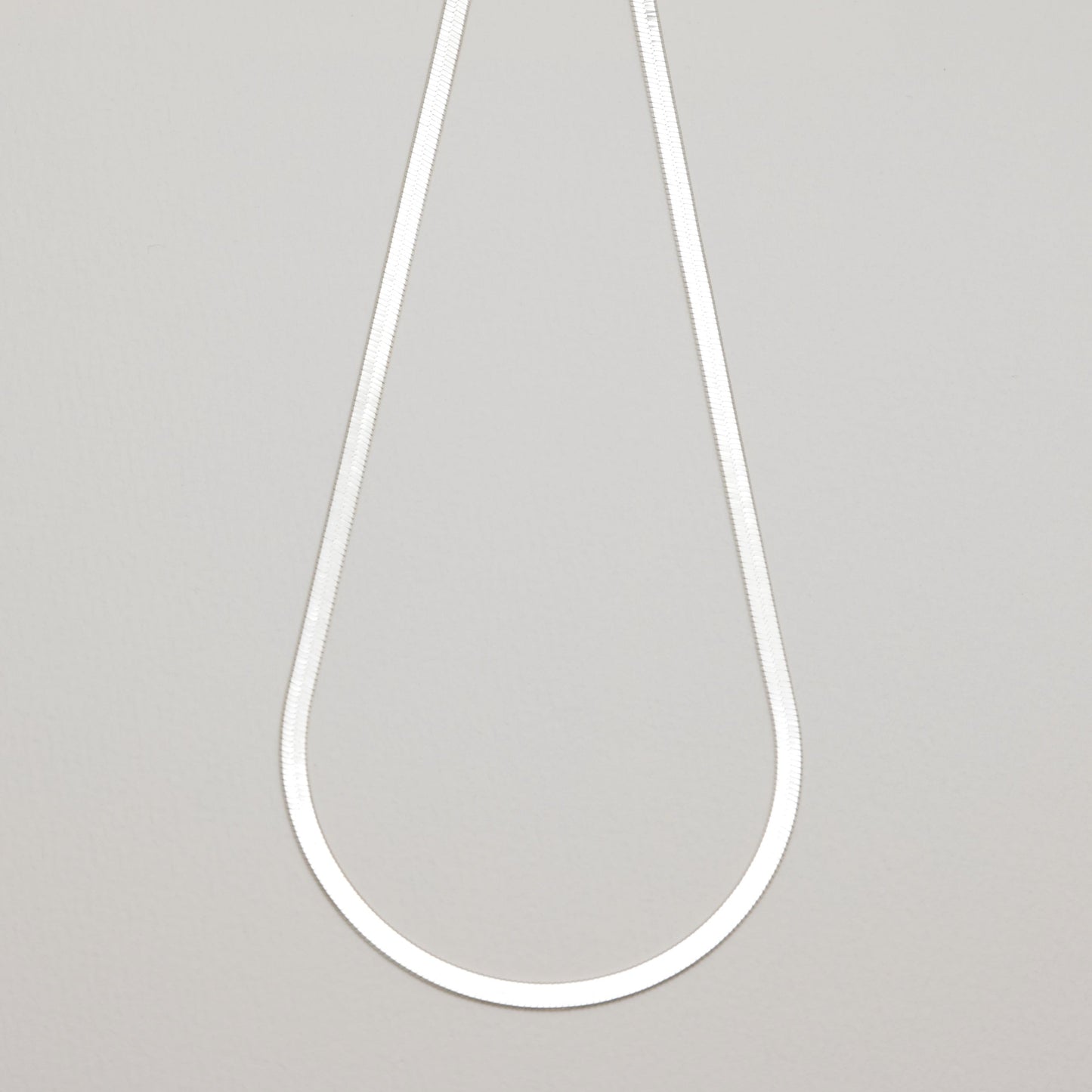 Full view of the Léa Herringbone Necklace laid flat in a teardrop shape against a neutral background.