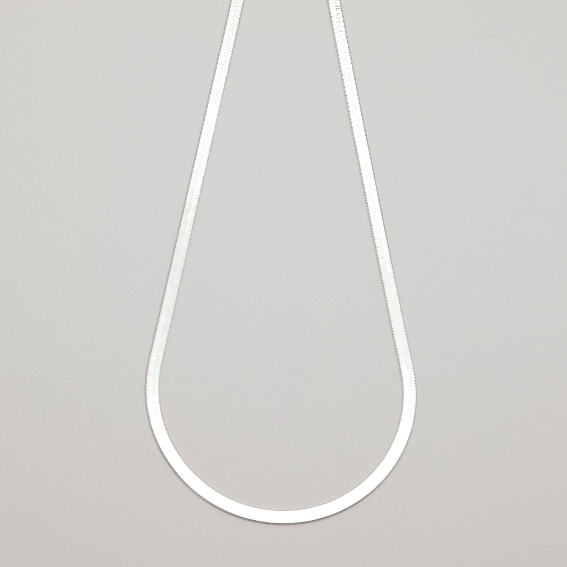 Full view of the Léa Herringbone Necklace laid flat in a teardrop shape against a neutral background.