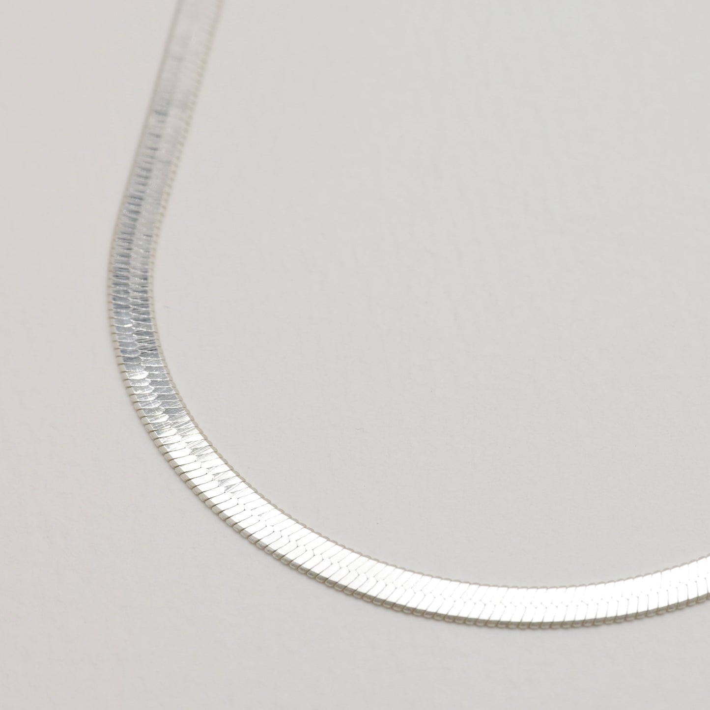 Angled detail of the necklace's curve showing its flat, polished silver links.