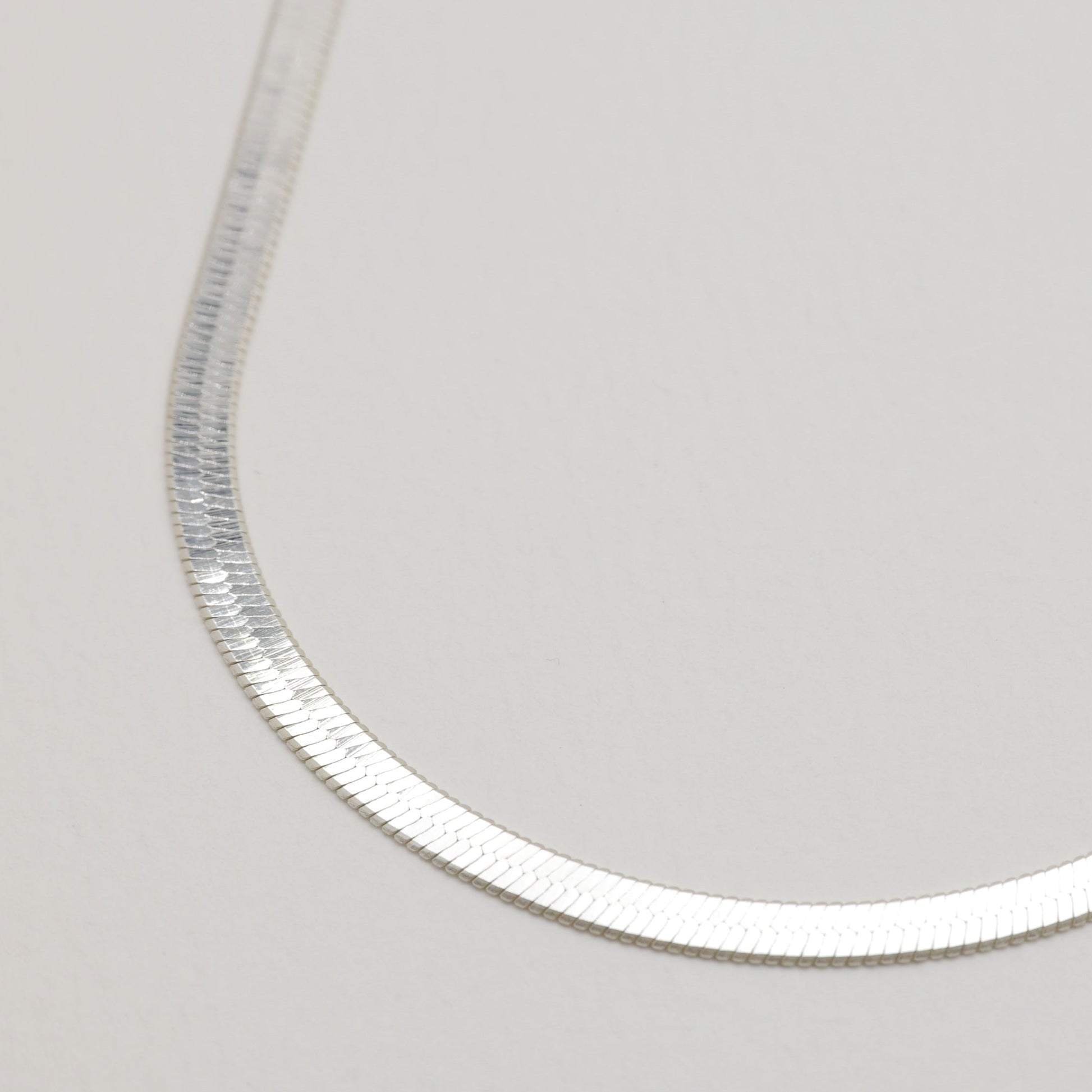 Angled detail of the necklace's curve showing its flat, polished silver links.