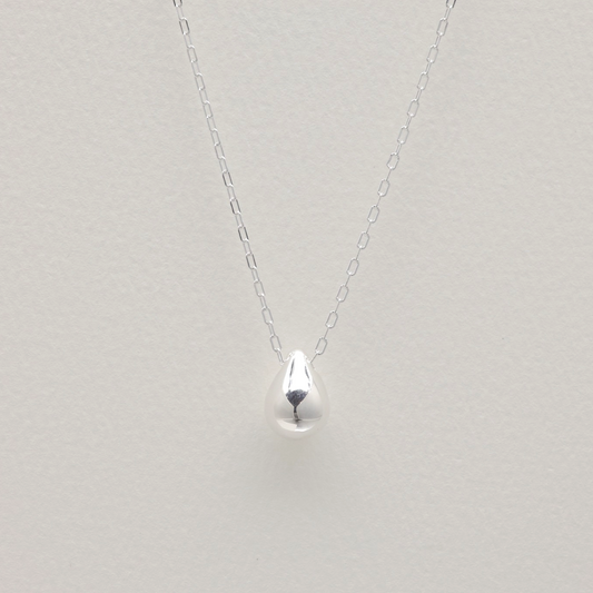Long sterling silver necklace with teardrop pendant on white background – minimalist sculptural jewelry design.