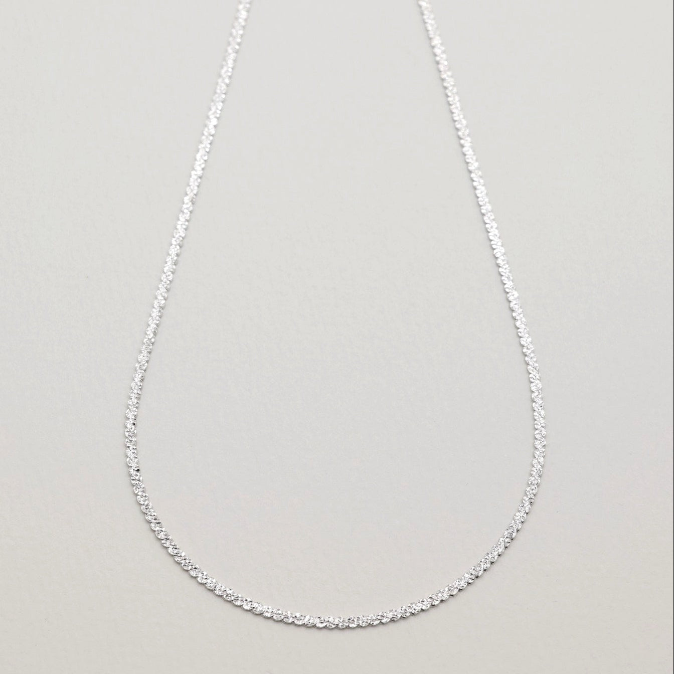 Full view of the Cléa Chain Necklace in sterling silver, laid in an oval shape against a soft grey background.