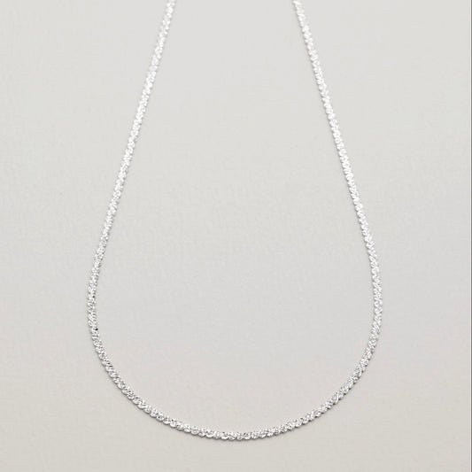 Full view of the Cléa Chain Necklace in sterling silver, laid in an oval shape against a soft grey background.