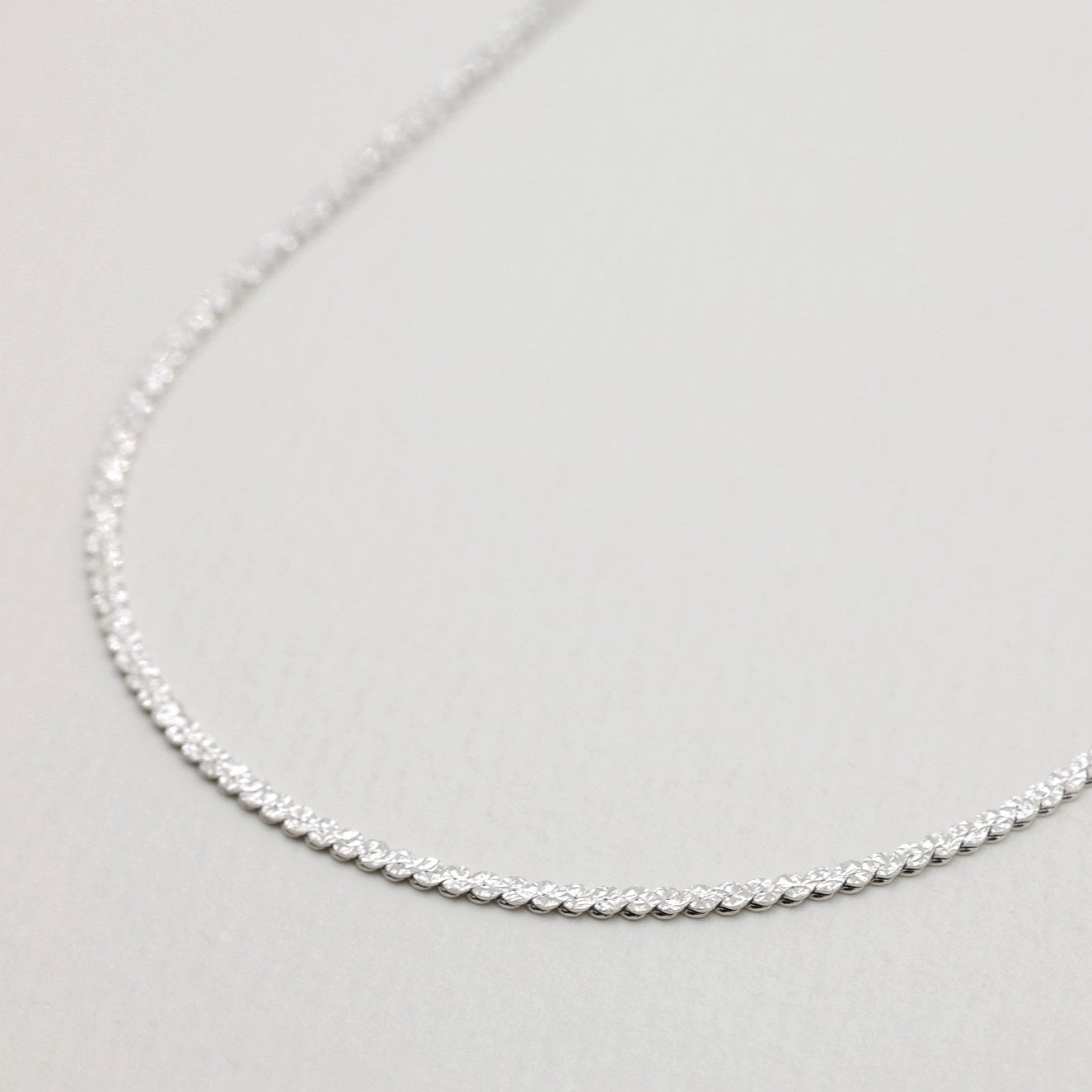 Close-up of the Cléa Chain Necklace showing its twisted reflective surface on the textured side.
