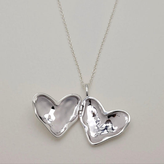 Open heart-shaped locket on a silver chain, showing smooth mirrored interior surfaces.