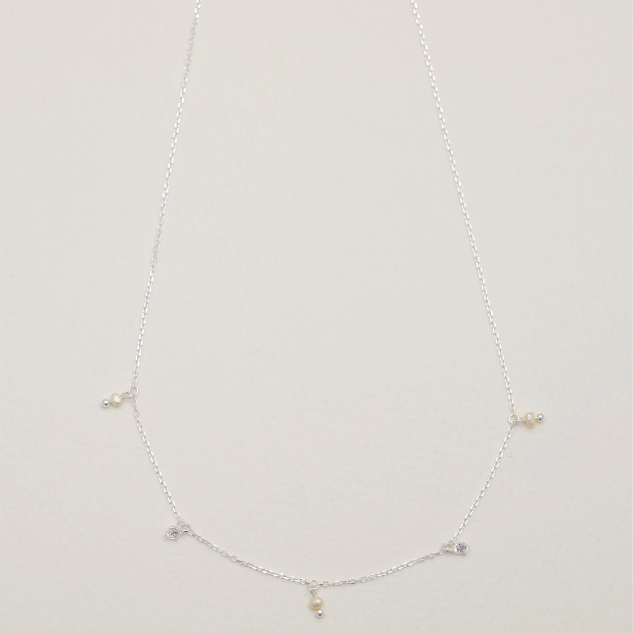 925 sterling silver necklace with cubic zirconia and natural pearl charms evenly spaced along a fine chain – MOA Jewelry flat lay
