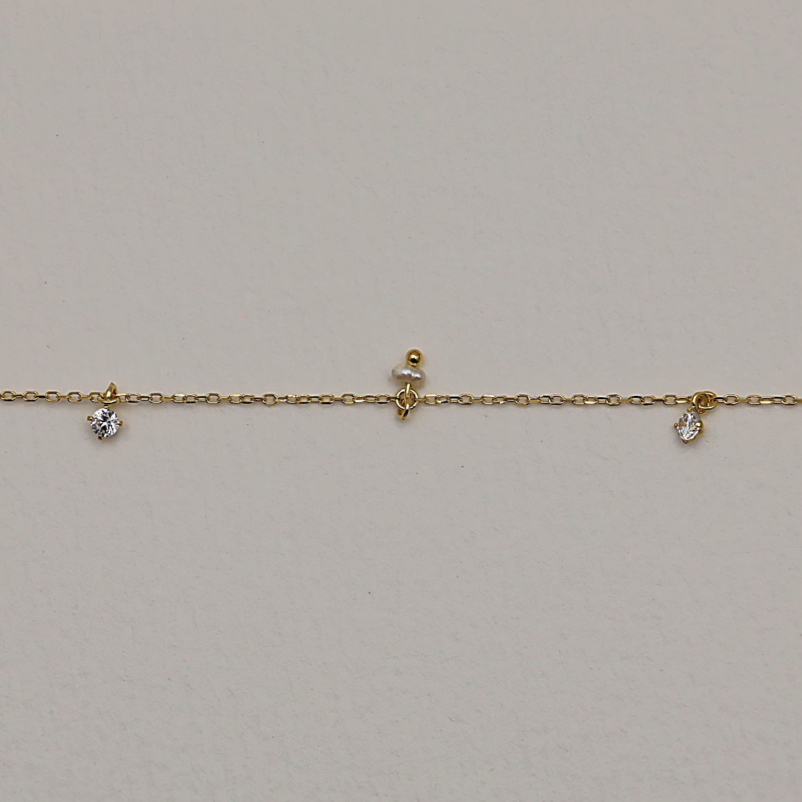 Close-up of MOA's Éliane Necklace showing polished gold vermeil chain and suspended pearl and cubic zirconia drops

