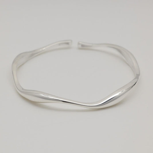 Image 1: Sculptural sterling silver cuff bracelet with fluid curves, displayed on a soft white background.