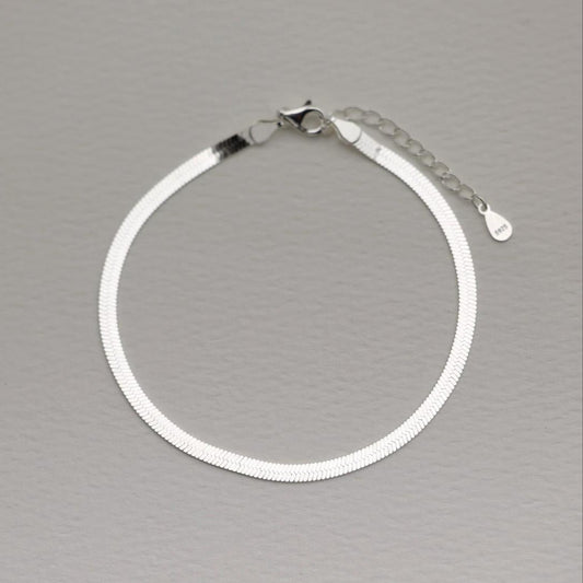 Flat herringbone bracelet in polished 925 sterling silver with extender chain, shown on a soft grey background.