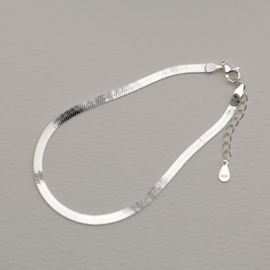Flat herringbone bracelet in polished 925 sterling silver with extender chain, shown on a soft grey background.