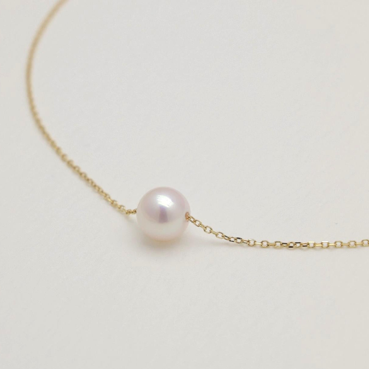 Delicate gold necklace with a single pearl on a light beige background