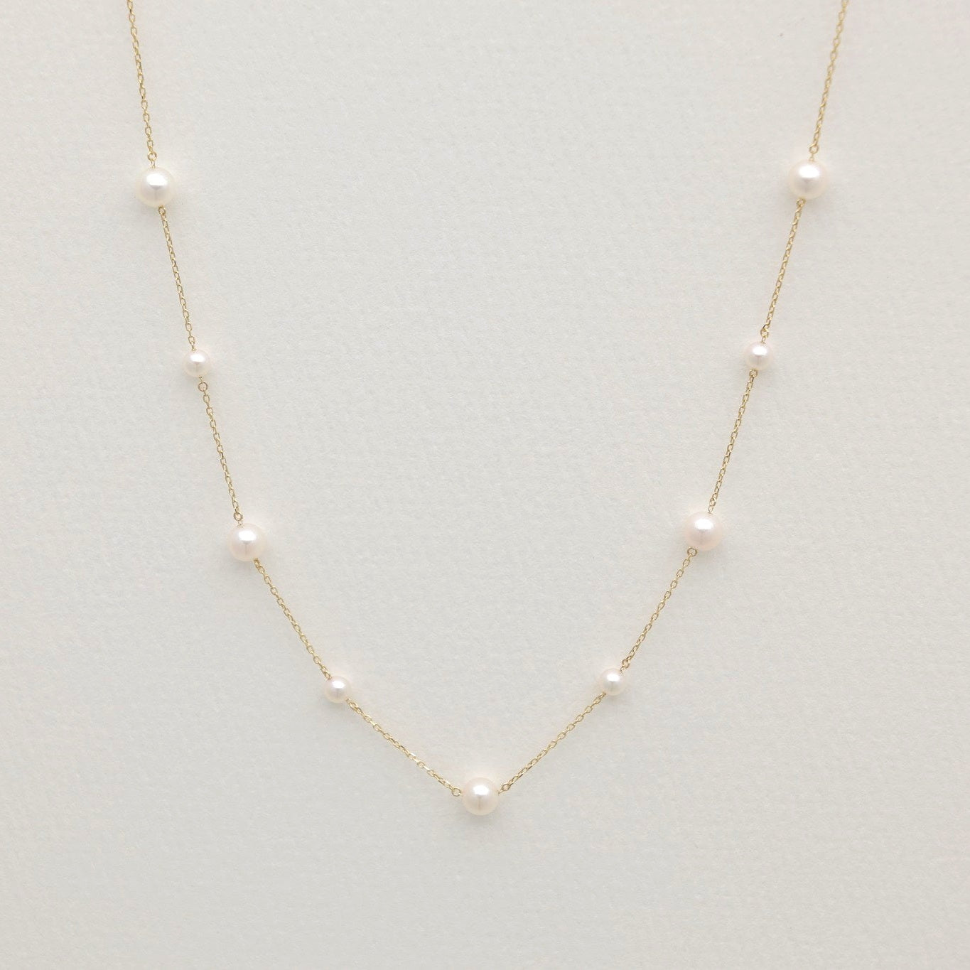 Gold necklace with small pearls on a light gray background