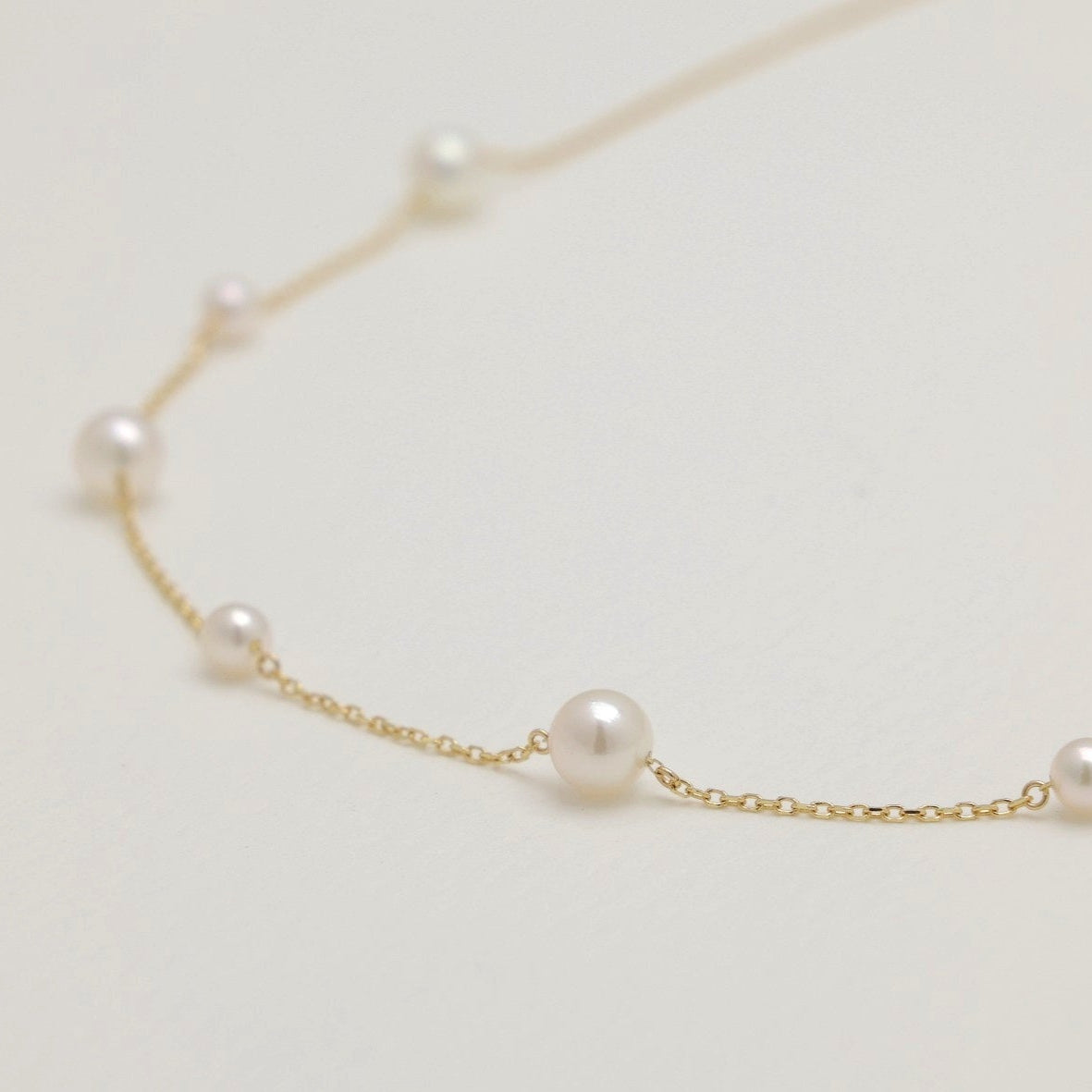 Delicate gold necklace with pearls on a light gray background