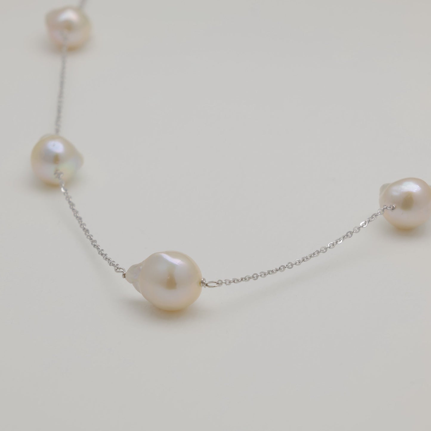 Close-up of baroque pearls and polished silver chain on cream background.
