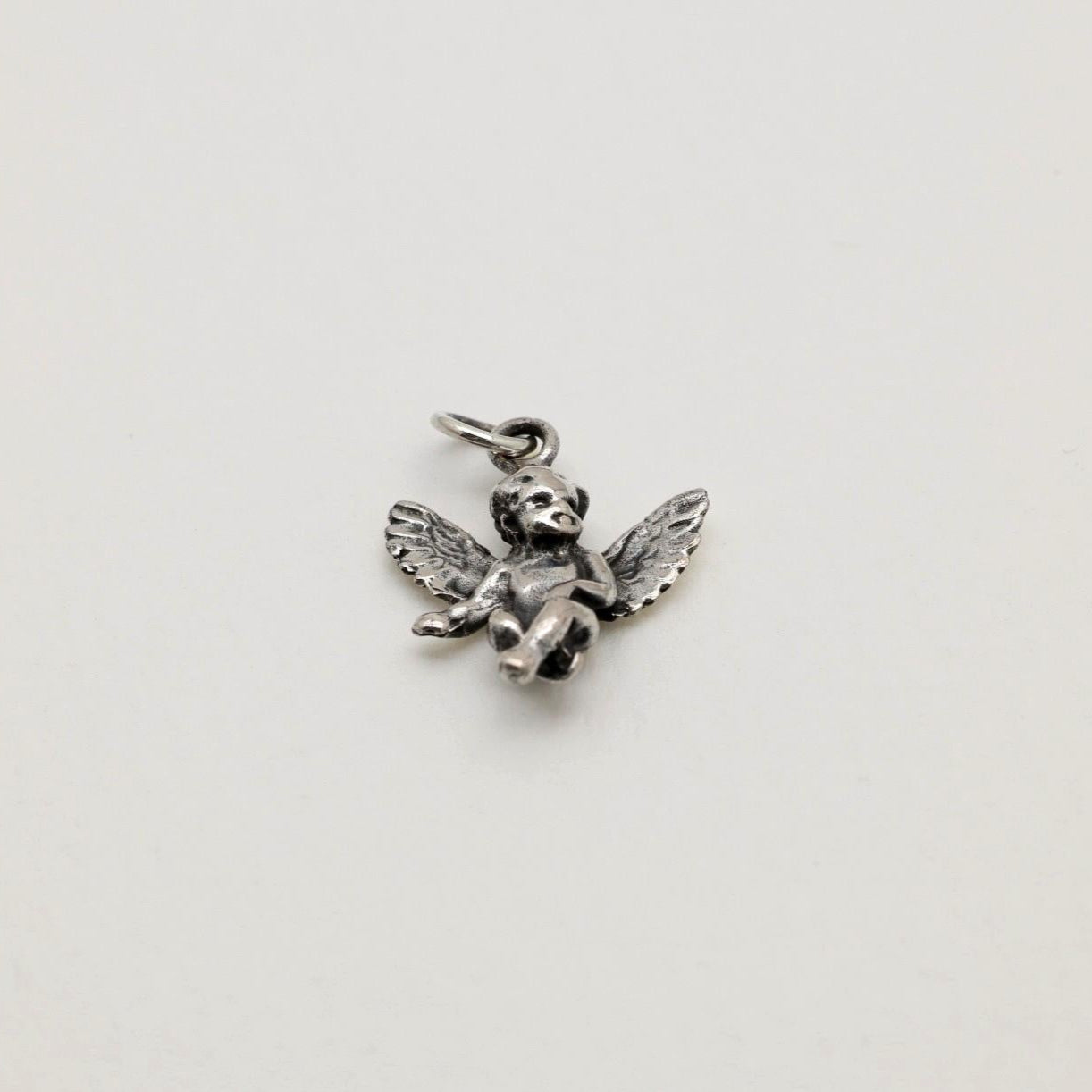 Sterling silver pendant in the shape of a seated cherub angel with wings, oxidized antique finish, photographed on a neutral background