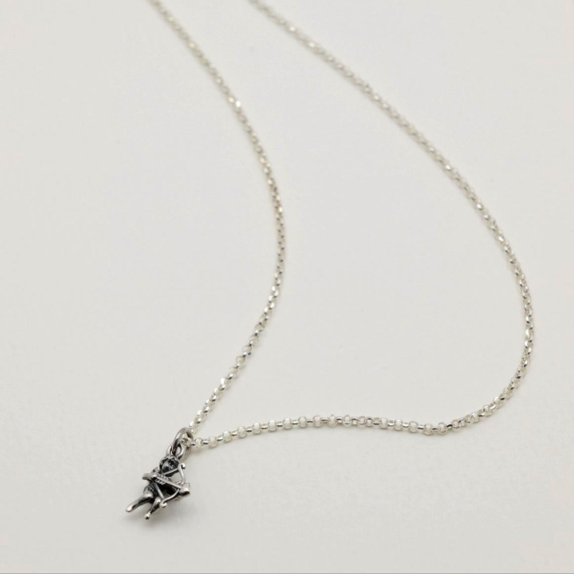 A sterling silver Cupid pendant charm featuring a bow and arrow, photographed on a soft white background.