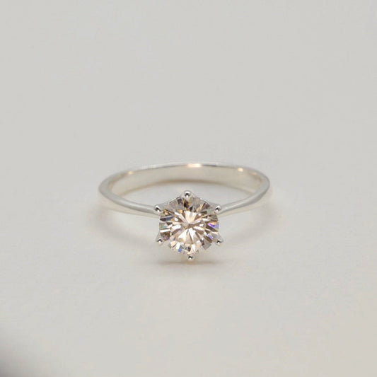 Round brilliant moissanite ring shown elevated on pale velvet cylinder
