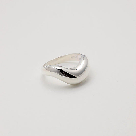 Sculptural sterling silver ring with a high-polish finish and fluid, wave-like design, set against a soft white background.