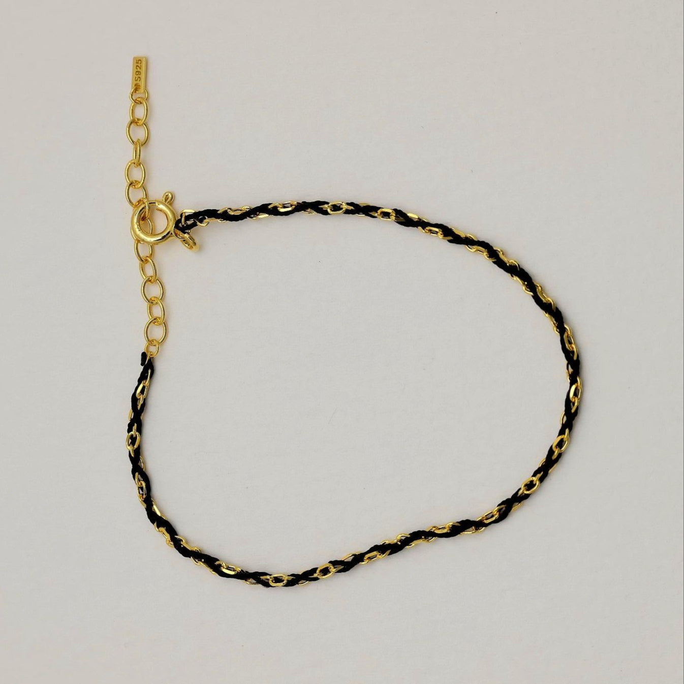 Gold vermeil bracelet with black cord laid flat, showing spring clasp and adjustable extender.

