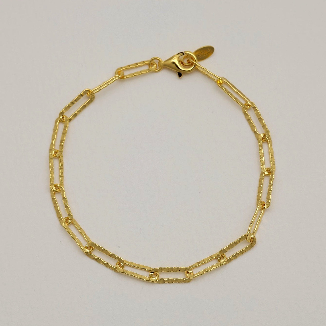 Sculptural gold link bracelet laid flat on a neutral background

