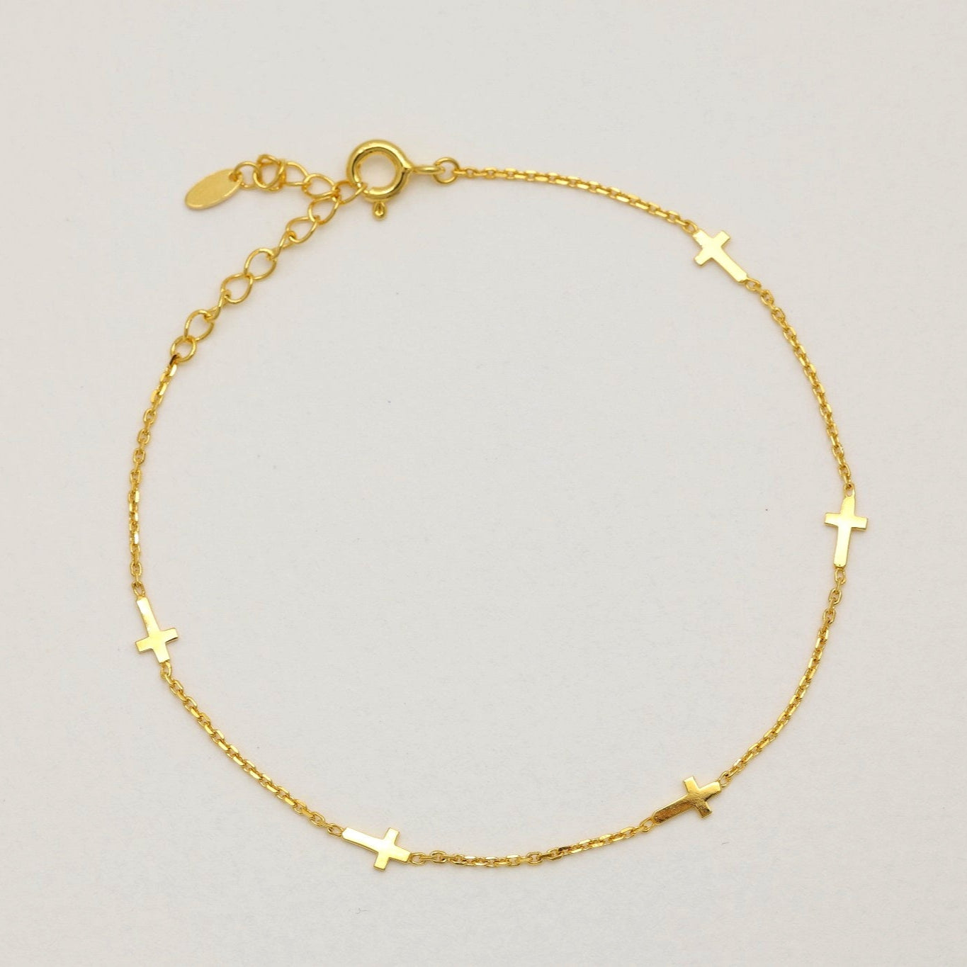 Gold vermeil bracelet with small cross charms laid flat on a light background

