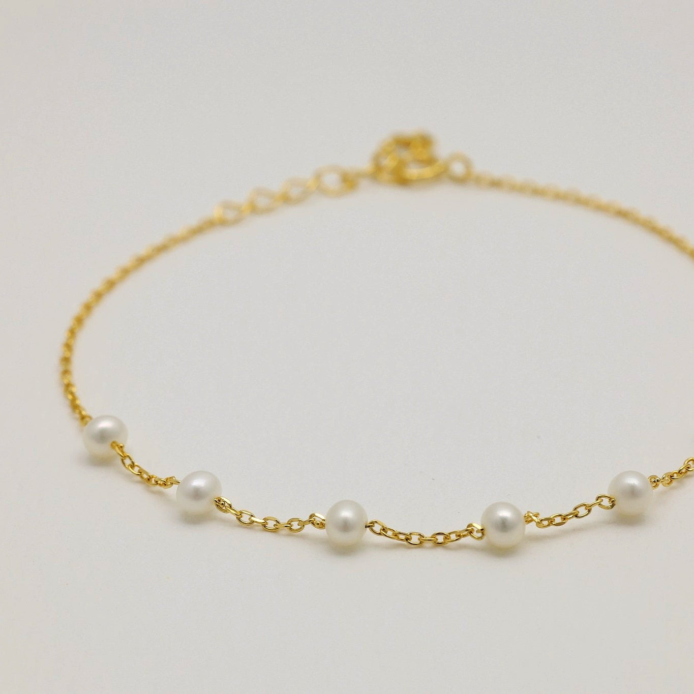 Angled view of a delicate gold vermeil bracelet featuring small white pearls, styled in a soft arc.

