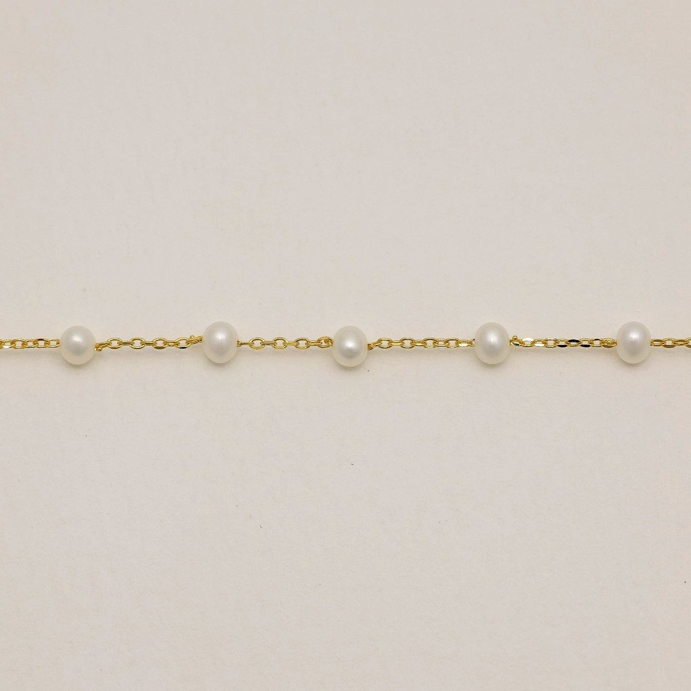 Gold vermeil chain bracelet with nine evenly spaced freshwater pearls laid flat on a light background.

