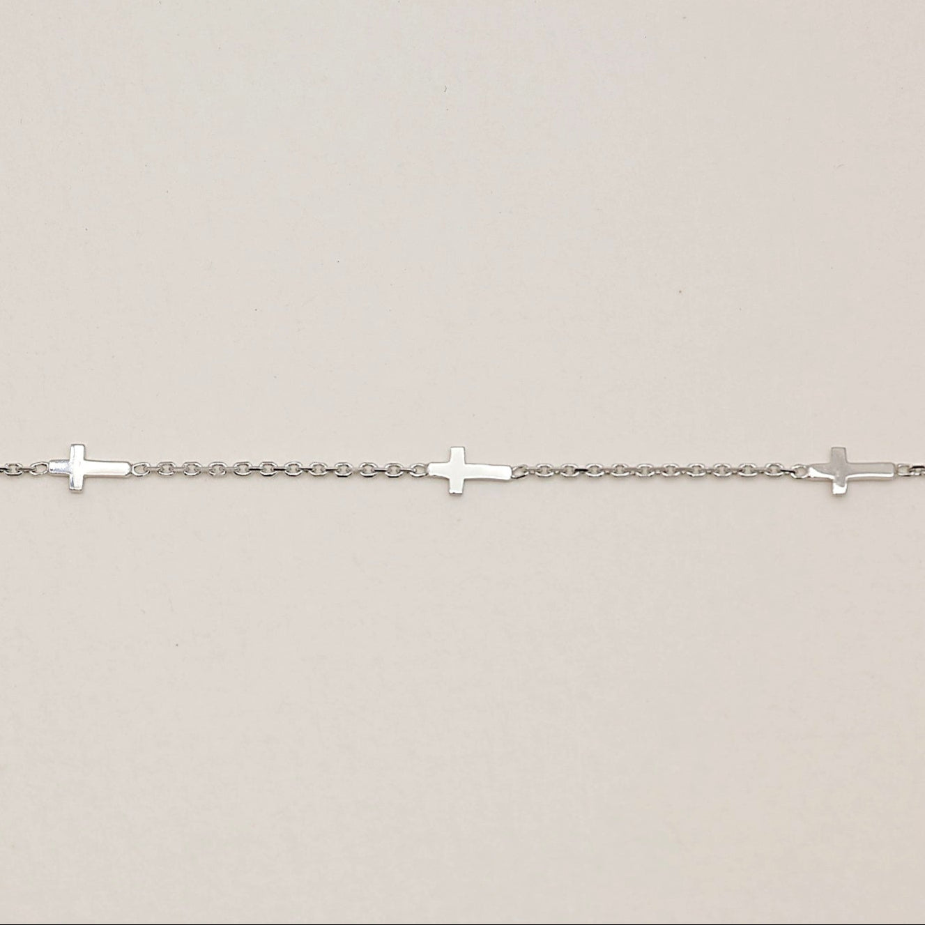 Close-up of cross motif sterling silver bracelet laid flat to show evenly spaced crosses and fine chain detail.

