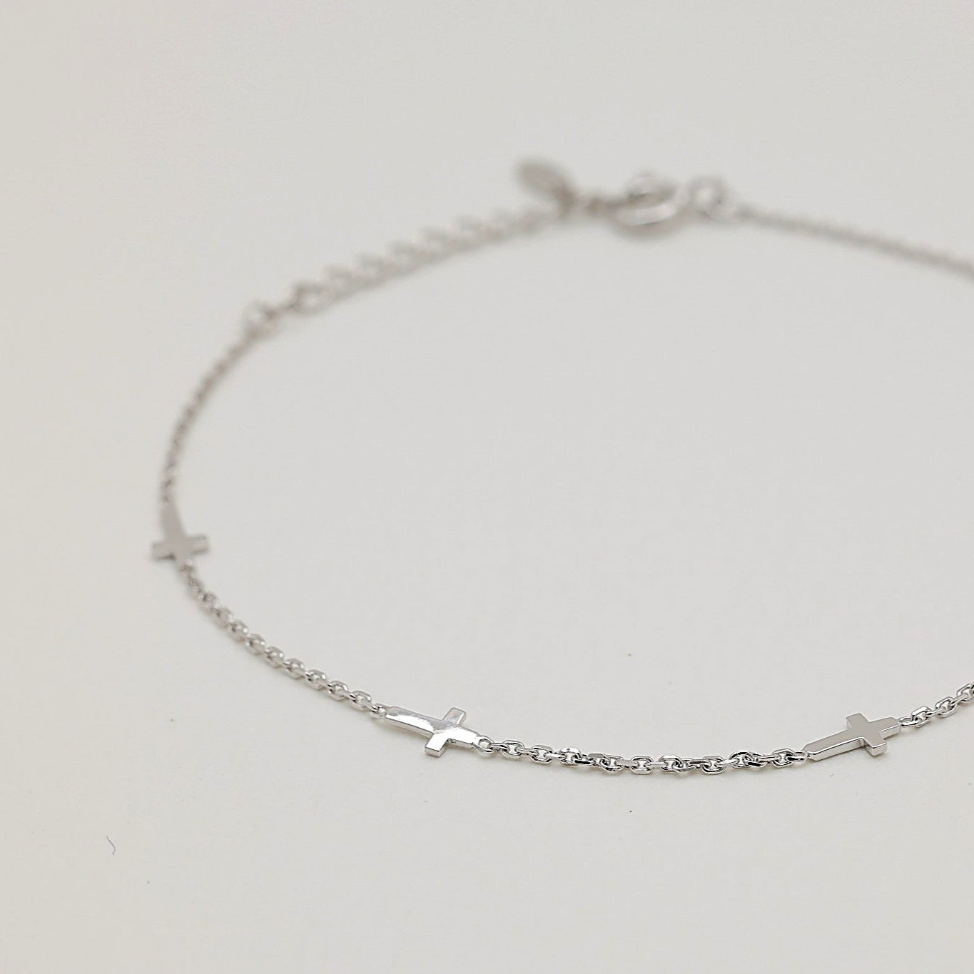 Sterling silver bracelet featuring evenly spaced small cross charms, displayed in a circular arrangement on a soft cream background.