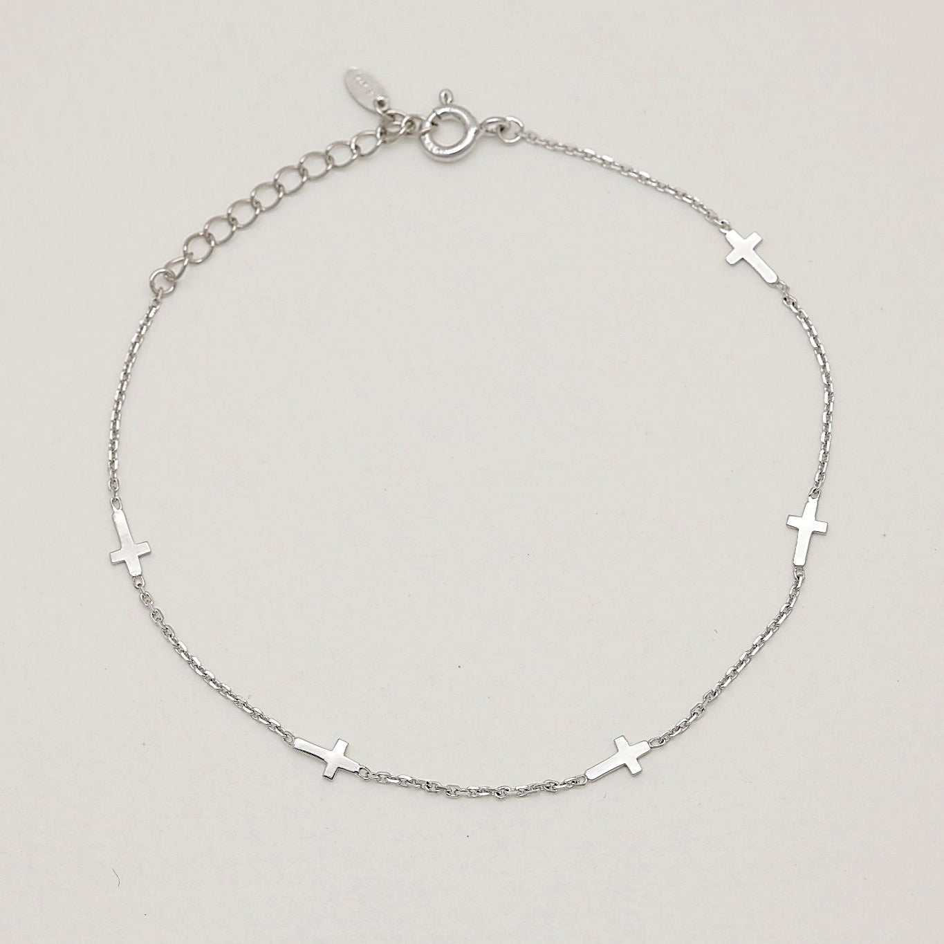 Minimalist cross charm bracelet in sterling silver, curved in a soft arc to highlight chain texture and charm spacing.

