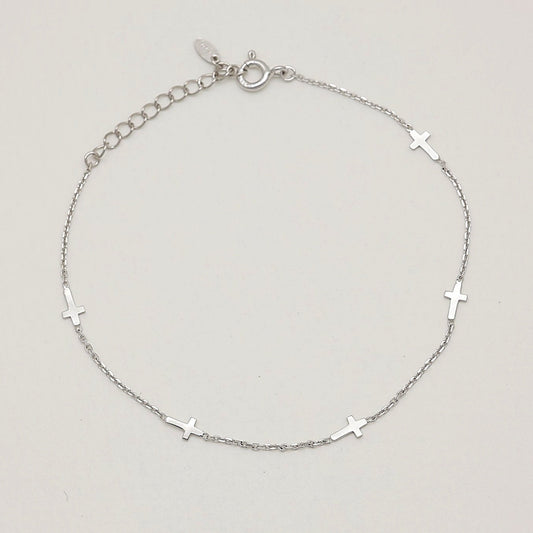 Minimalist cross charm bracelet in sterling silver, curved in a soft arc to highlight chain texture and charm spacing.


