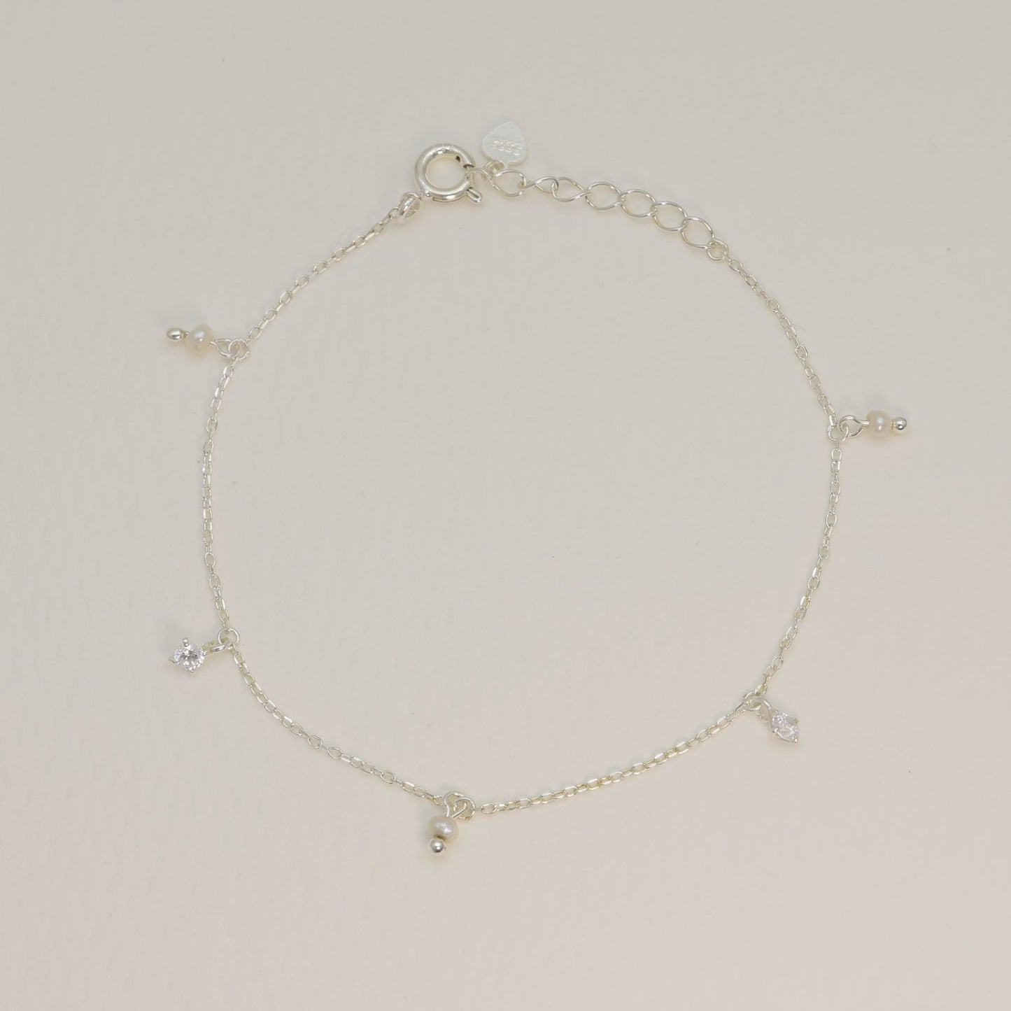Sterling silver charm bracelet laid flat to reveal symmetrical arrangement of pearl and cubic zirconia charms along the chain.

