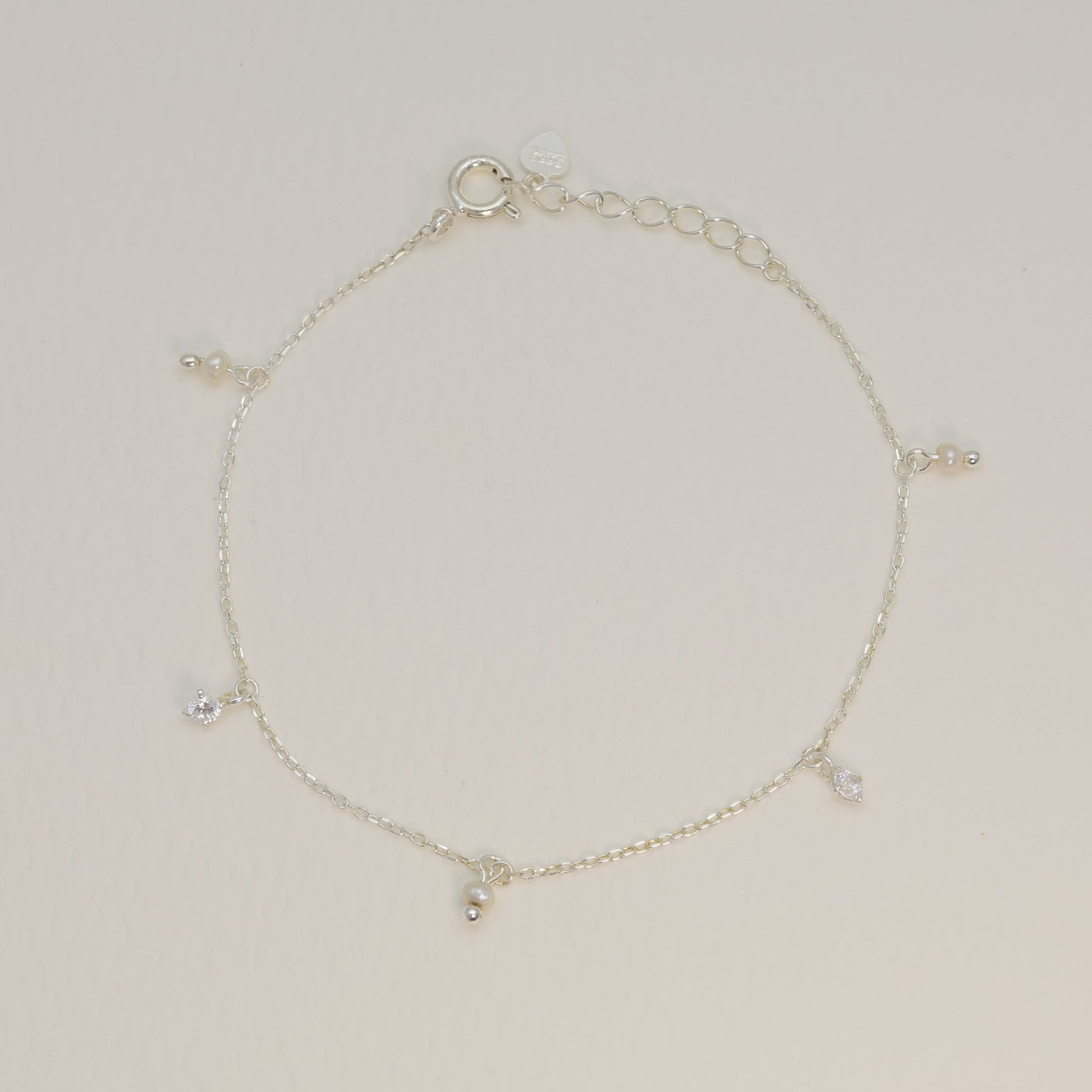 Sterling silver charm bracelet laid flat to reveal symmetrical arrangement of pearl and cubic zirconia charms along the chain.

