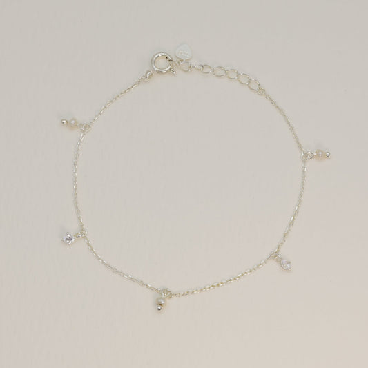 Sterling silver charm bracelet laid flat to reveal symmetrical arrangement of pearl and cubic zirconia charms along the chain.

