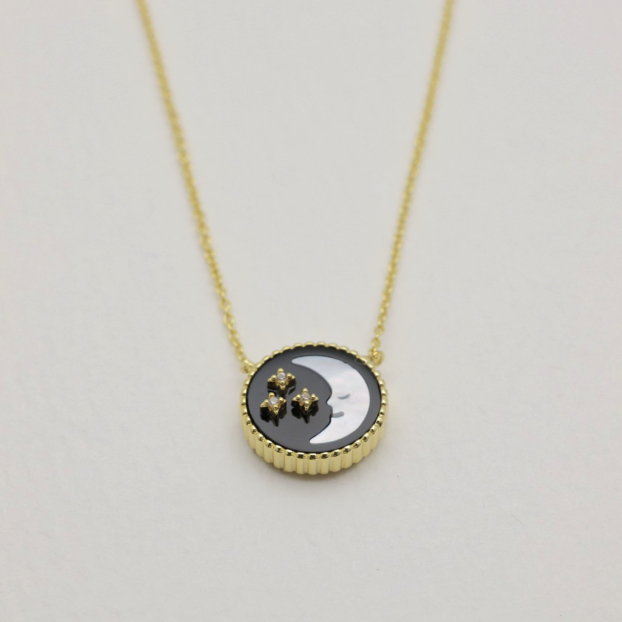 Close-up of the moon side of a gold vermeil necklace pendant with cubic zirconia stars on black and white enamel.