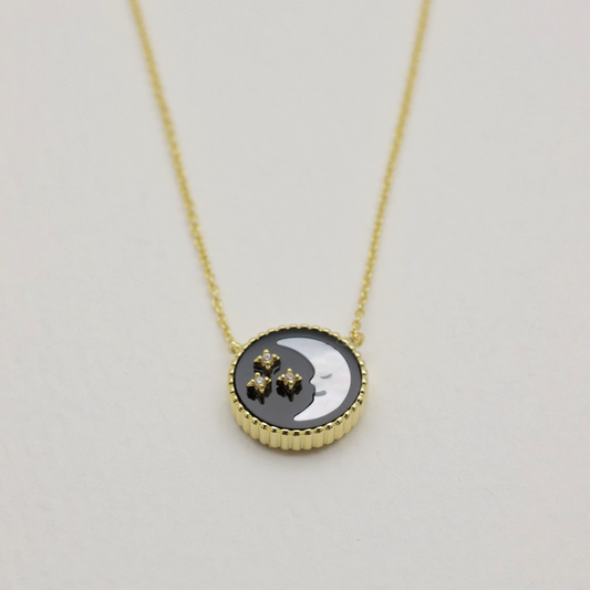 Close-up of the moon side of a gold vermeil necklace pendant with cubic zirconia stars on black and white enamel.