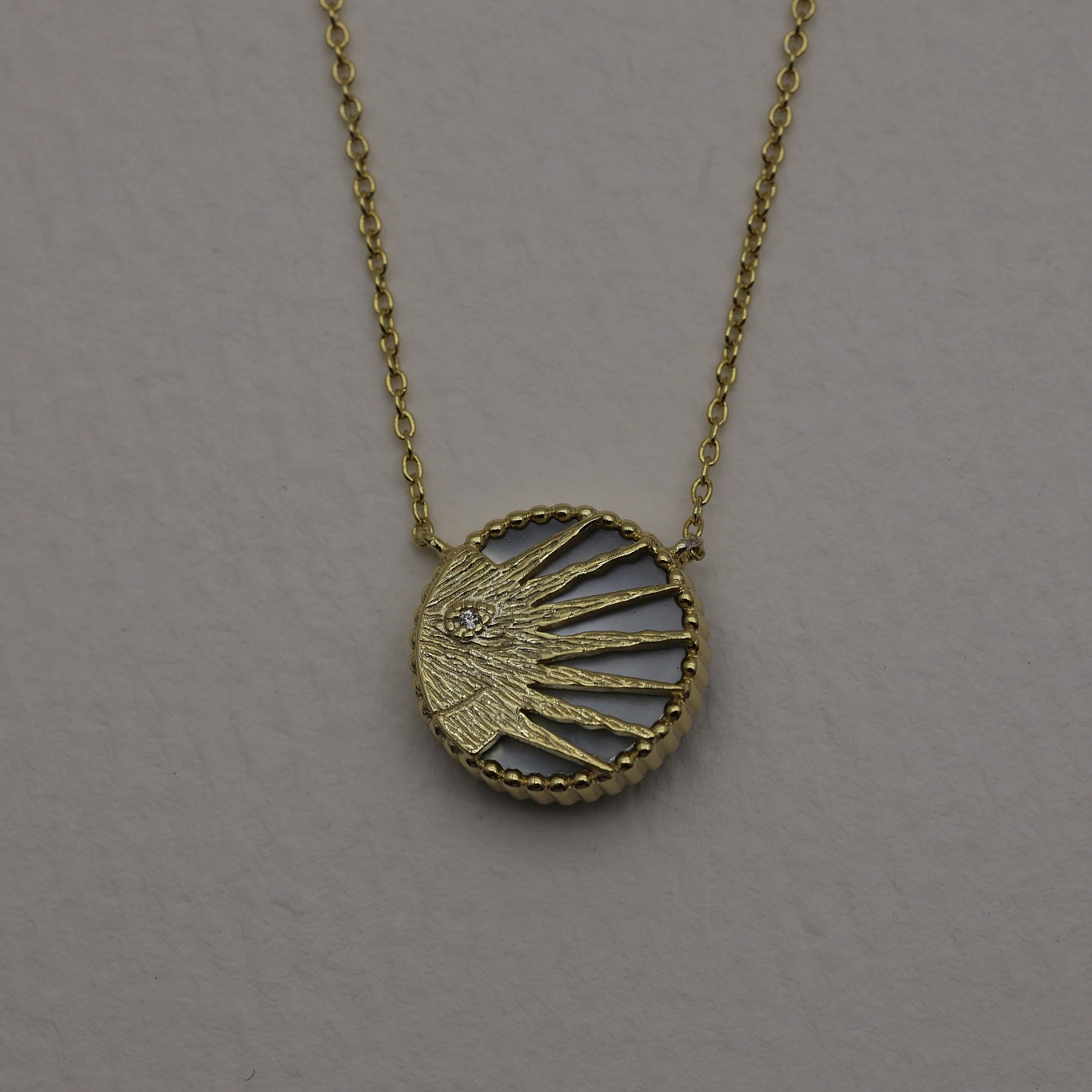 Close-up of the sun side of the same pendant, featuring a radiating gold design with a single cubic zirconia at the center.