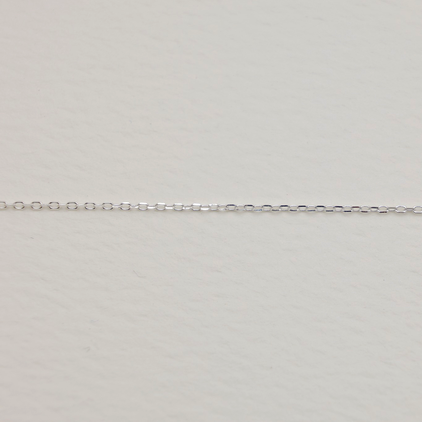 Close-up of a delicate sterling silver chain necklace with a pavé circle pendant lying flat against a soft white background.
