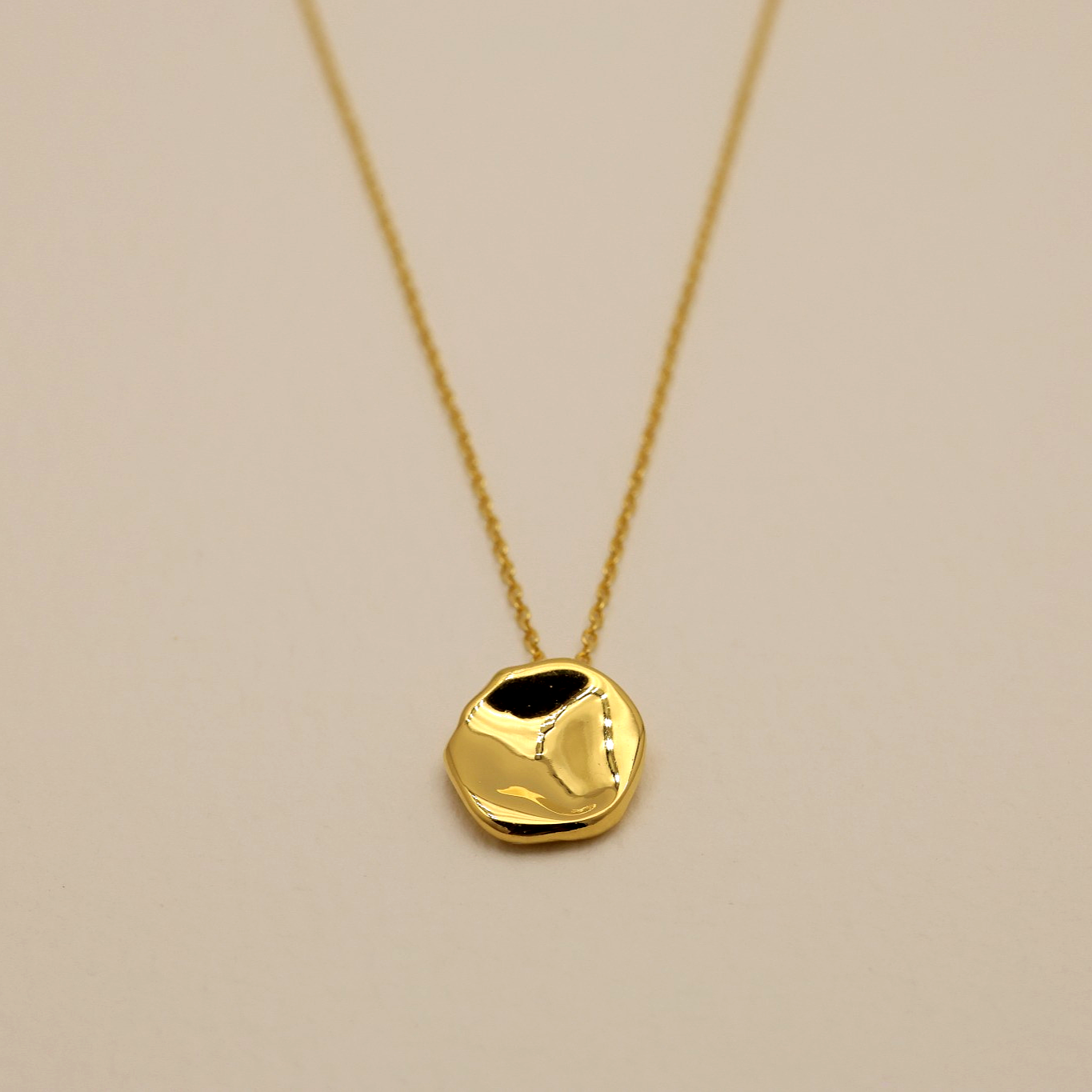 Close-up of polished sculptural disc pendant in 18K gold vermeil